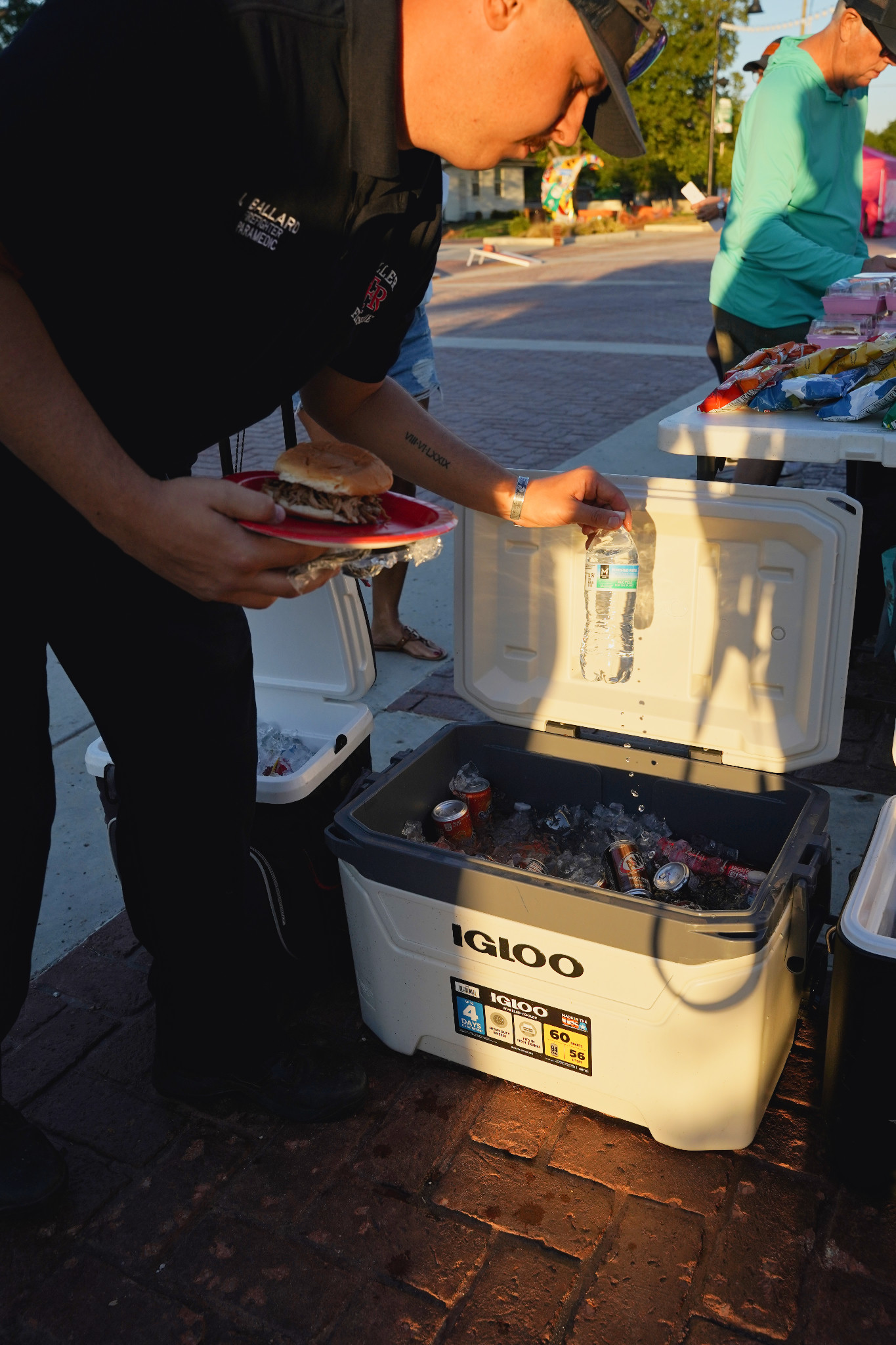 A member of Keller Fire Rescue holding a plate of food takes a bottle of water from a cooler.