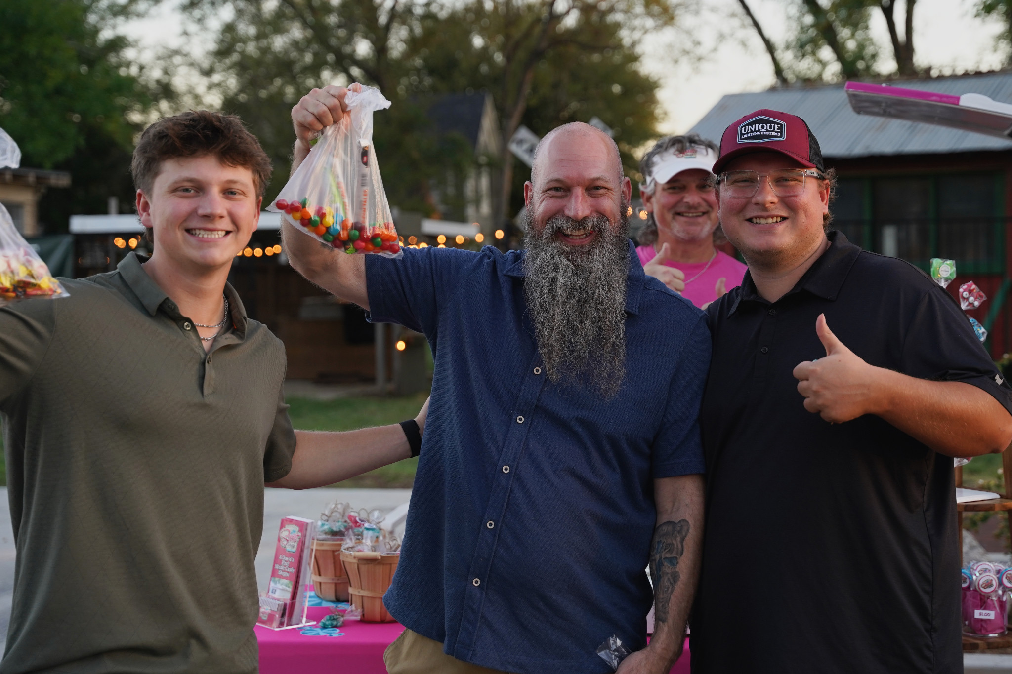 Neighbors smile for a photo beside the candy display, with one guest holding up a bag of colorful candy.